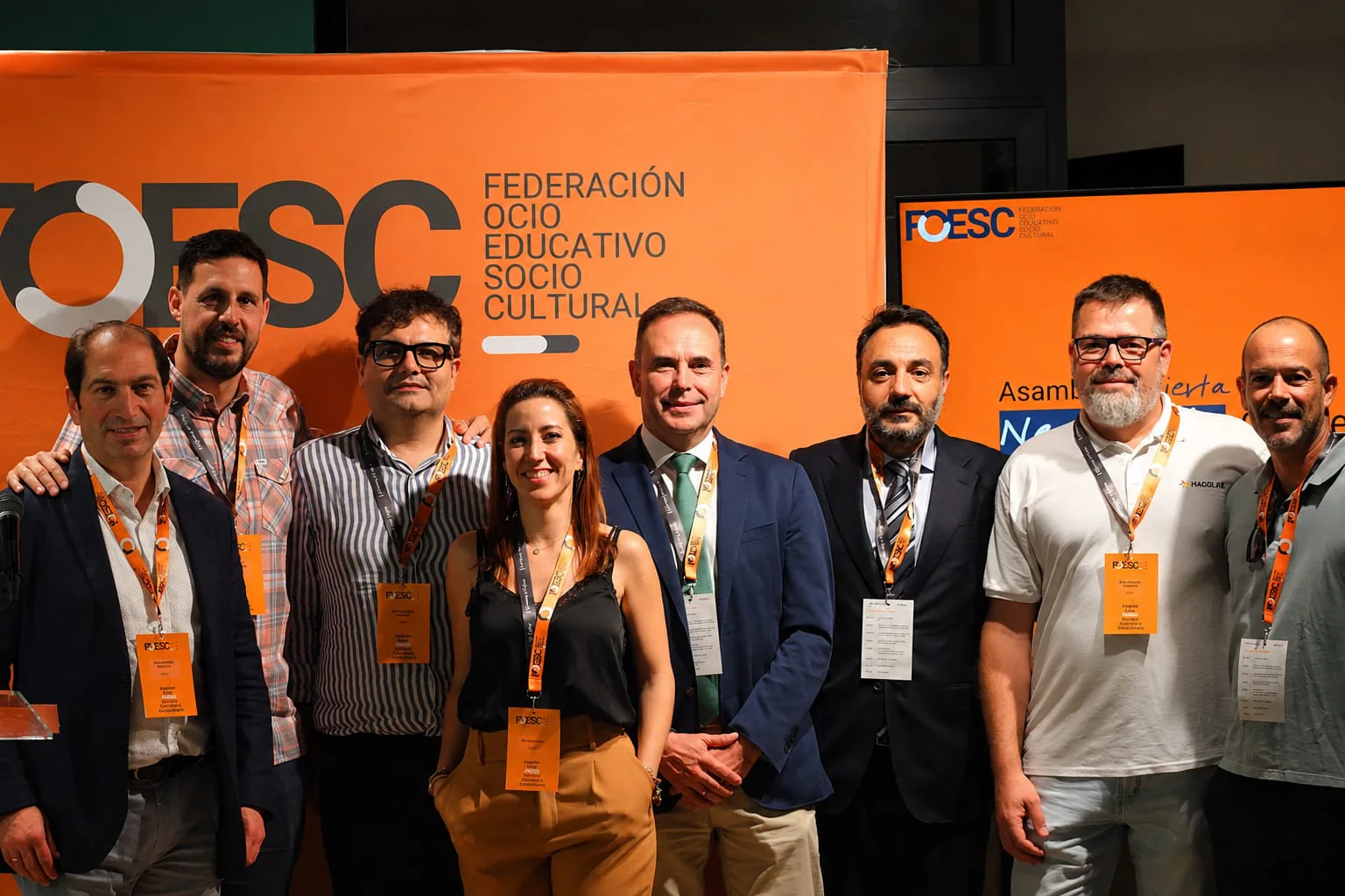 Un grup d’assistents posa davant un fons taronja de FOESC.